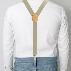 Person wearing beige suspenders over a white shirt and blue jeans on a light gray background