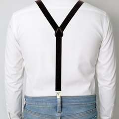 Person wearing suspenders over a white shirt and blue jeans on a plain background